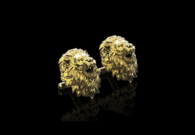 May include: A pair of gold lion head cufflinks. The lion heads are detailed and realistic, with a textured mane and open mouths.