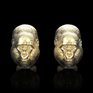 Könnte beinhalten: Ein Paar goldfarbene Manschettenknöpfe in Form eines Gorillakopfes. Die Manschettenknöpfe sind mit einer strukturierten Oberfläche detailliert und haben ein realistisches Gorillagesicht.