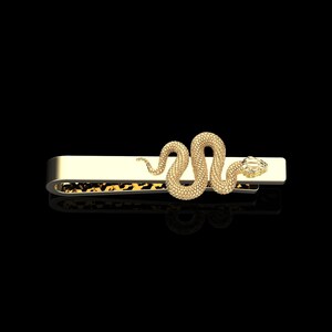 Könnte beinhalten: Ein goldener Krawattenclip mit einem Schlangendesign. Die Schlange ist zusammengerollt und hat einen Diamanten im Maul.