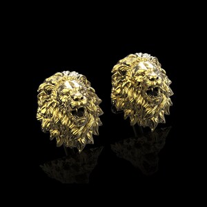 May include: A pair of gold lion head cufflinks. The lion heads are facing forward with their mouths open and their teeth showing.