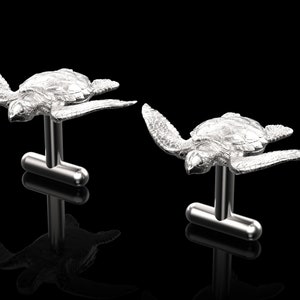 May include: A pair of silver cufflinks featuring a detailed, three-dimensional design of a sea turtle in flight.