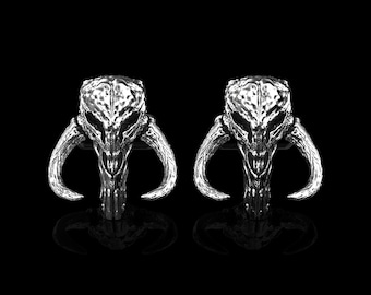 May include: A pair of silver cufflinks featuring a detailed Mandalorian skull design with horns.