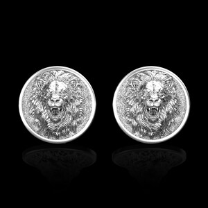 May include: A pair of silver cufflinks featuring a lion's head design. The lion's head is in relief and has a detailed mane.