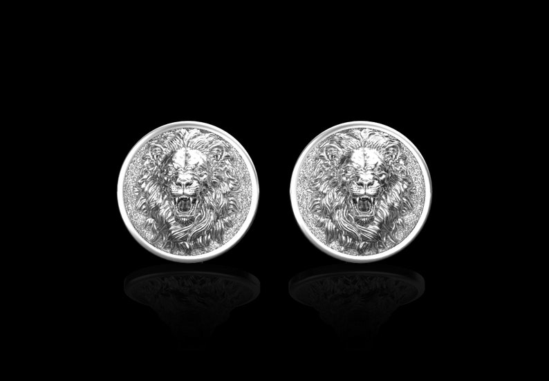 May include: A pair of silver cufflinks featuring a lion's head design. The lion's head is in relief and has a detailed mane.