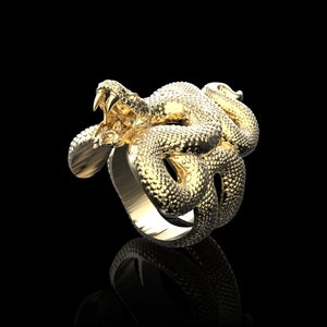 May include: A gold-colored ring featuring a detailed snake design. The snake is coiled around the ring band, with its head raised and fangs bared.