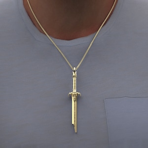May include: A gold chain necklace with a sword pendant. The sword is detailed with intricate carvings and has a pointed tip.