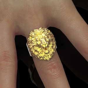 Puede incluir: Un anillo de oro con un dise&ntilde;o detallado de cabeza de le&oacute;n. La boca del le&oacute;n est&aacute; abierta y su melena est&aacute; esculpida de forma intrincada.