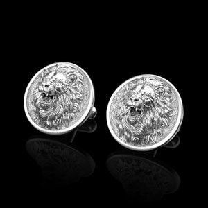 May include: A pair of silver cufflinks with a lion head design. The lion's face is detailed and realistic, with a mane of hair.