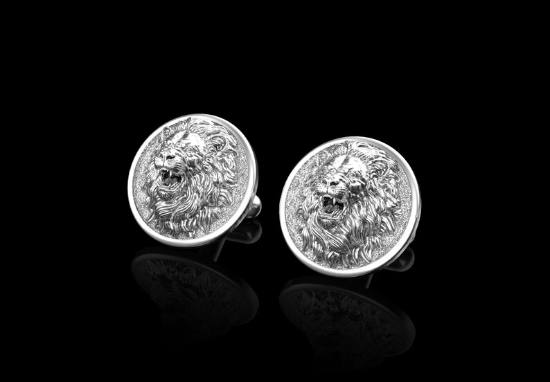 May include: A pair of silver cufflinks with a lion head design. The lion's face is detailed and realistic, with a mane of hair.