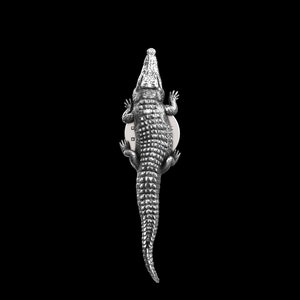 May include: A silver alligator figurine with a textured, scaly surface. The alligator is posed with its mouth open and its tail curled up.