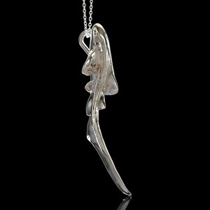 May include: A silver pendant necklace with a detailed, abstract design resembling a stylized bird or wing. The pendant is suspended from a delicate silver chain.