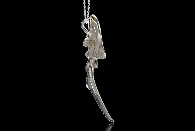May include: A silver pendant necklace with a detailed, abstract design resembling a stylized bird or wing. The pendant is suspended from a delicate silver chain.