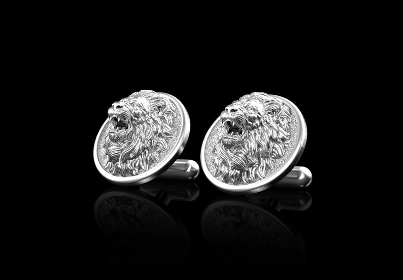 May include: A pair of silver cufflinks featuring a detailed lion head design. The lion's mouth is open and its mane is intricately sculpted.