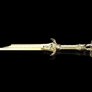 May include: A gold sword pendant necklace with a detailed design and a chain. The pendant is approximately 5 cm long.