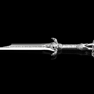 K&ouml;nnte beinhalten: Eine silberne Schwertpendantkette mit einem detaillierten Sch&auml;del-Design am Griff. Das Schwert ist an einer silbernen Kette befestigt.