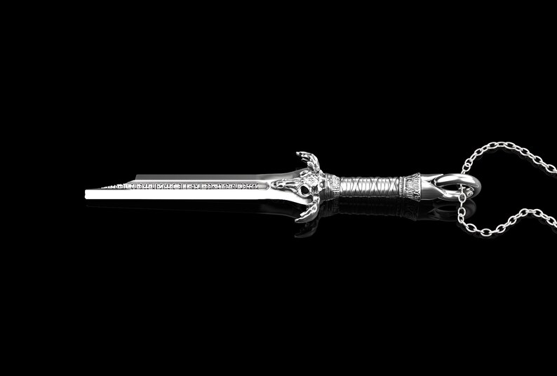 K&ouml;nnte beinhalten: Eine silberne Schwertpendantkette mit einem detaillierten Sch&auml;del-Design am Griff. Das Schwert ist an einer silbernen Kette befestigt.
