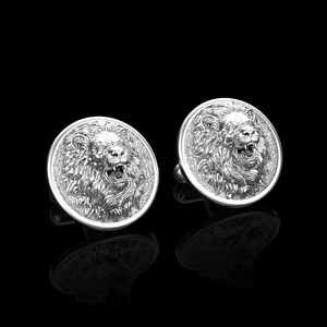 May include: A pair of silver cufflinks featuring a detailed lion head design. The lion's mouth is open and its mane is intricately sculpted.