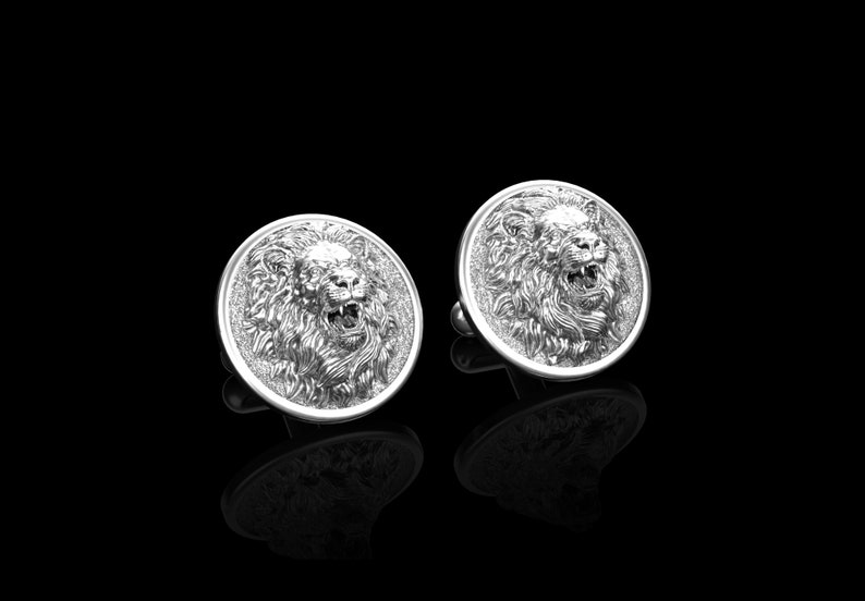 May include: A pair of silver cufflinks featuring a detailed lion head design. The lion's mouth is open and its mane is intricately sculpted.