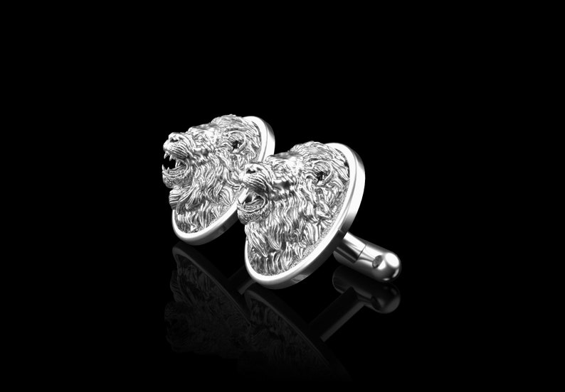 May include: A pair of silver cufflinks with a detailed lion head design. The lion heads are facing forward with their mouths open.