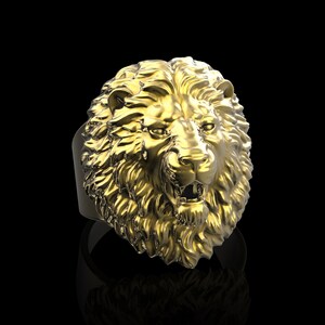 Puede incluir: Un anillo de cabeza de le&oacute;n de oro con un dise&ntilde;o detallado. La boca del le&oacute;n est&aacute; abierta y sus dientes son visibles.