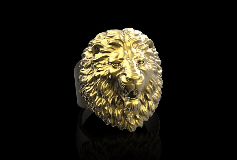 Puede incluir: Un anillo de cabeza de le&oacute;n de oro con un dise&ntilde;o detallado. La boca del le&oacute;n est&aacute; abierta y sus dientes son visibles.