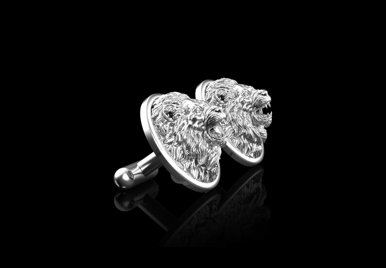 May include: A pair of silver cufflinks featuring detailed lion head designs. The lion heads are facing forward with their mouths open.