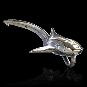 May include: A silver shark sculpture with a shiny, reflective finish. The shark is posed in a swimming position with its tail raised and its mouth open.