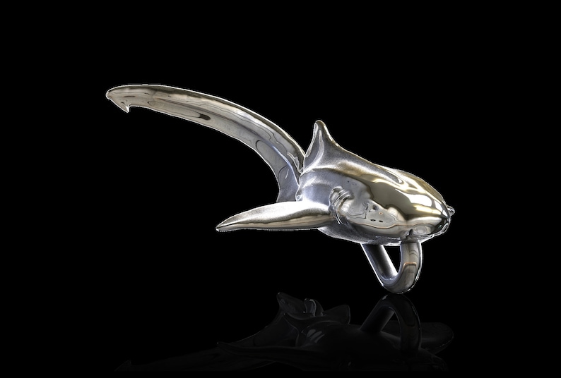 May include: A silver shark sculpture with a shiny, reflective finish. The shark is posed in a swimming position with its tail raised and its mouth open.