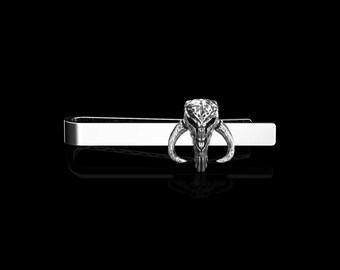 May include: A silver tie clip with a Mandalorian skull design.