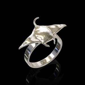 May include: A silver ring featuring a detailed manta ray design. The ring is polished and has a smooth finish.