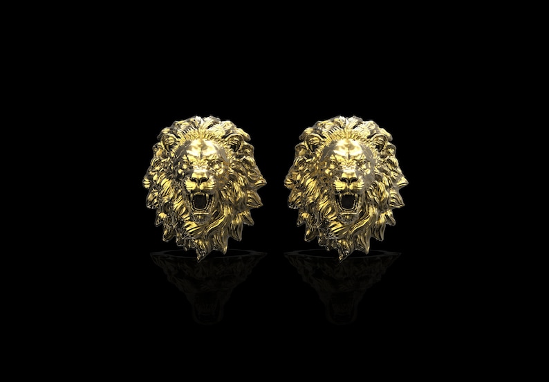 May include: A pair of gold lion head earrings. The lion heads are facing forward with their mouths open and their teeth showing.