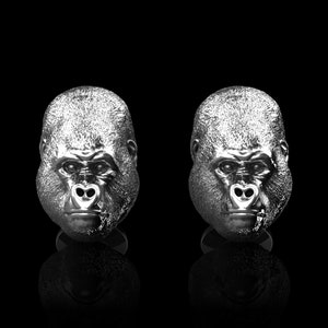 Könnte beinhalten: Ein Paar silberne Manschettenknöpfe mit einem detaillierten Gorillakopf-Design. Die Manschettenknöpfe sind ein einzigartiges und stilvolles Accessoire für jeden Anlass.