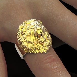 Puede incluir: Un anillo de oro con cabeza de le&oacute;n con un dise&ntilde;o detallado. El anillo se lleva en un dedo.