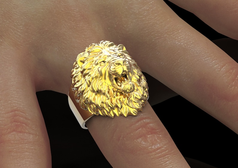 Puede incluir: Un anillo de oro con cabeza de le&oacute;n con un dise&ntilde;o detallado. El anillo se lleva en un dedo.