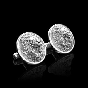 May include: A pair of silver cufflinks with a lion head design. The lion heads are facing forward with their mouths open.