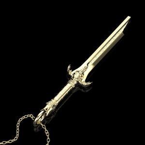 May include: A gold-coloured sword pendant necklace with a detailed design. The sword has a pointed tip and a decorative handle. The necklace is made of a gold chain.