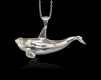 May include: A silver pendant in the shape of an orca whale, hanging from a silver chain. The pendant is highly polished and reflects light.