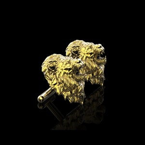 May include: A pair of gold lion head cufflinks. The lion heads are facing forward with their mouths open, as if roaring. The cufflinks are made of a shiny metal and have a detailed design.