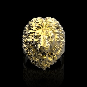 Puede incluir: Un anillo de cabeza de le&oacute;n de oro con un dise&ntilde;o detallado. La melena del le&oacute;n est&aacute; esculpida de forma intrincada y el anillo est&aacute; sobre un fondo negro.