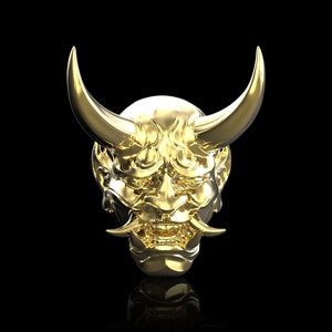 May include: A golden Oni mask with curved horns and intricate facial details. The mask has a menacing expression with sharp teeth and a furrowed brow. The mask is set against a black background, highlighting its metallic sheen.
