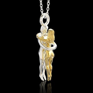 May include: A silver chain necklace with a gold and silver pendant depicting two figures embracing. The figures are intertwined and appear to be a couple.