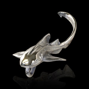 May include: A silver shark sculpture with a shiny, polished finish. The shark is posed in a swimming position with its tail curled up.
