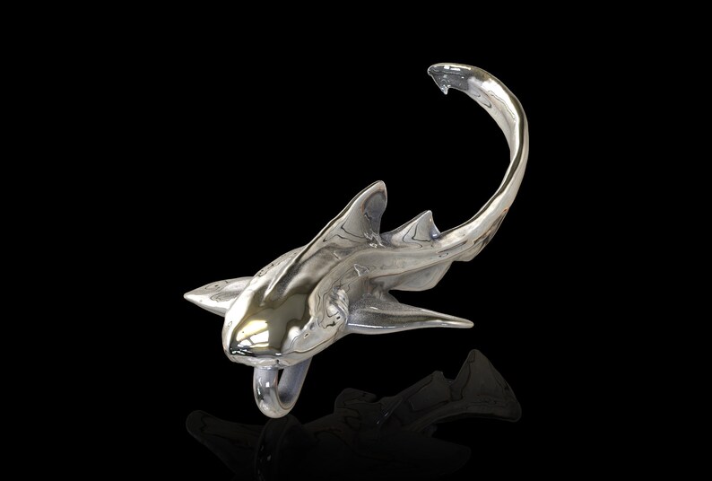 May include: A silver shark sculpture with a shiny, polished finish. The shark is posed in a swimming position with its tail curled up.