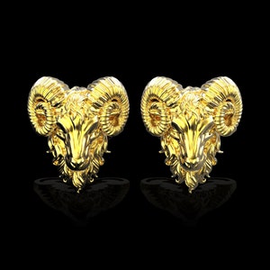 Puede incluir: Un par de pendientes de color dorado con un diseño detallado de cabeza de carnero. Los pendientes son una pieza llamativa con detalles intrincados y un motivo animal clásico.