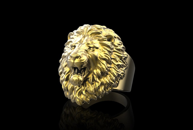 Puede incluir: Un anillo de cabeza de le&oacute;n de oro con un dise&ntilde;o detallado. La boca del le&oacute;n est&aacute; abierta y sus dientes son visibles. El anillo est&aacute; hecho de una banda gruesa de metal.