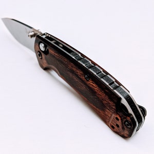 May include: A brown and black pocket knife with a wood handle and a stainless steel blade.
