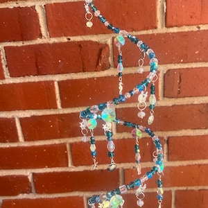 May include: A spiral-shaped hanging mobile constructed from wire, adorned with various blue and clear glass beads. The structure features dangling charms shaped like seahorses, seashells, and starfish, creating a multi-layered decorative piece.