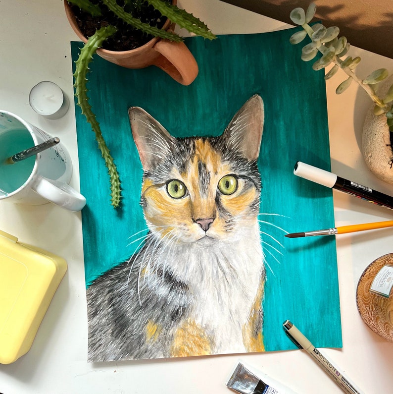 K&ouml;nnte beinhalten: Ein Gem&auml;lde einer dreifarbigen Katze mit gr&uuml;nen Augen auf einem t&uuml;rkisfarbenen Hintergrund. Die Katze schaut direkt auf den Betrachter.