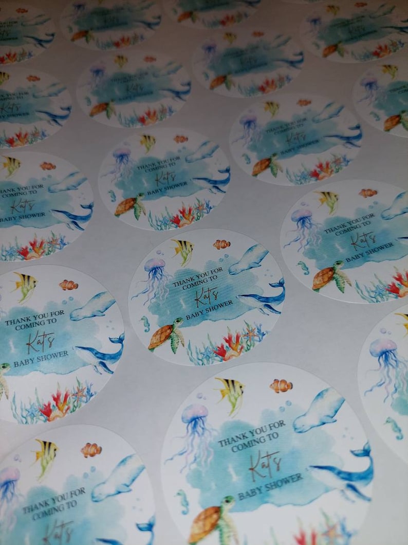 May include: Round blue and white thank you stickers with a watercolor design of sea life, including a whale, jellyfish, and a turtle. The text on the stickers reads "Thank you for coming to Kats Baby Shower".