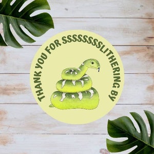 May include: A round sticker with a yellow background and a green snake illustration. The text on the sticker reads "Thank you for ssssssslithering by".